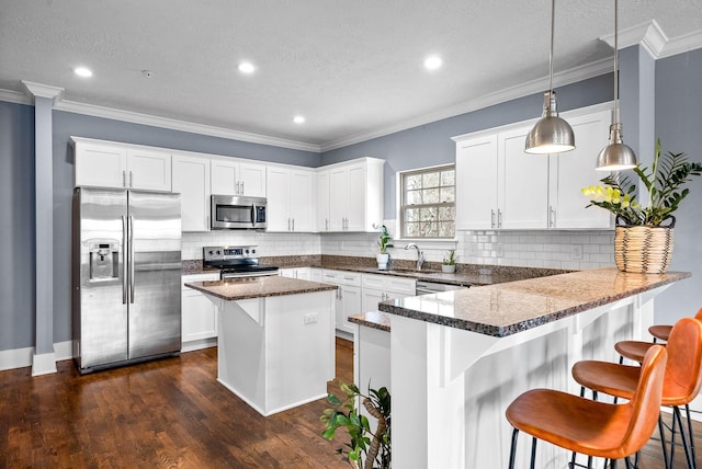 kitchen with pendant lighting, white cabinets, appliances with stainless steel finishes, a center island, and crown molding