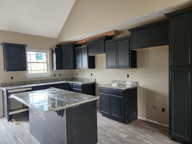 kitchen with dark cabinetry, a kitchen island, light wood finished floors, and light stone countertops