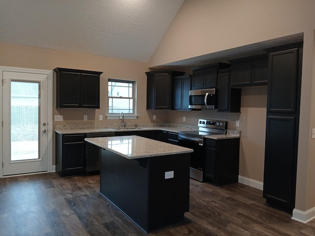 kitchen with light stone counters, a center island, appliances with stainless steel finishes, vaulted ceiling, and a sink