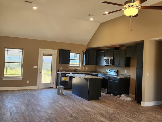 kitchen featuring appliances with stainless steel finishes, a healthy amount of sunlight, light stone counters, and a center island