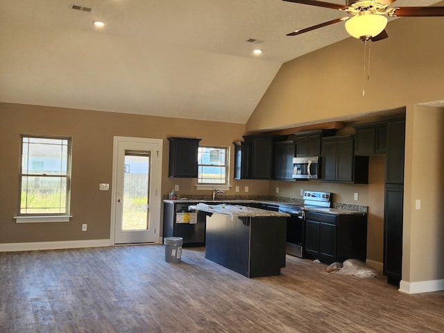 kitchen with a kitchen island, visible vents, dark cabinetry, appliances with stainless steel finishes, and light stone countertops