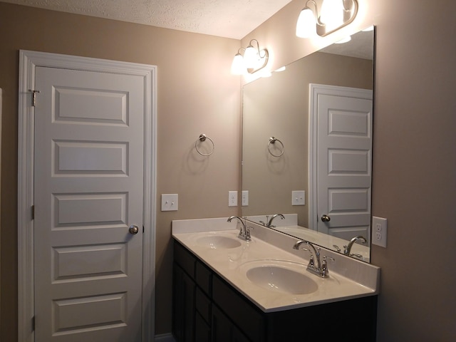 full bath featuring a textured ceiling, double vanity, and a sink