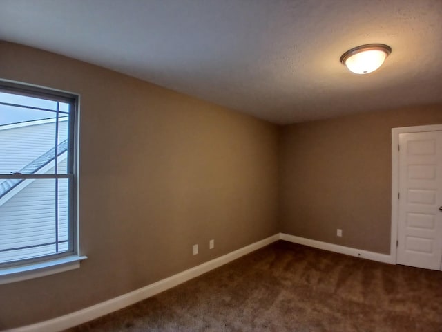 empty room featuring plenty of natural light, dark carpet, and baseboards