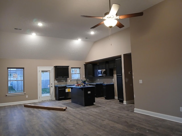 kitchen featuring dark wood-style flooring, stainless steel microwave, open floor plan, a kitchen island, and dark cabinetry