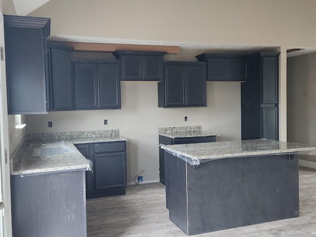 kitchen with lofted ceiling, light stone counters, baseboards, a center island, and light wood finished floors