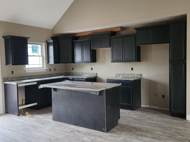 kitchen featuring light wood finished floors, light stone counters, dark cabinets, and a center island