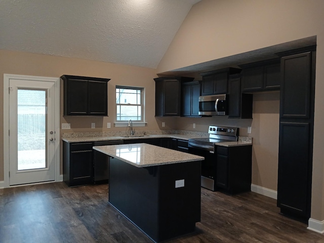 kitchen featuring lofted ceiling, a center island, light stone countertops, stainless steel appliances, and a sink