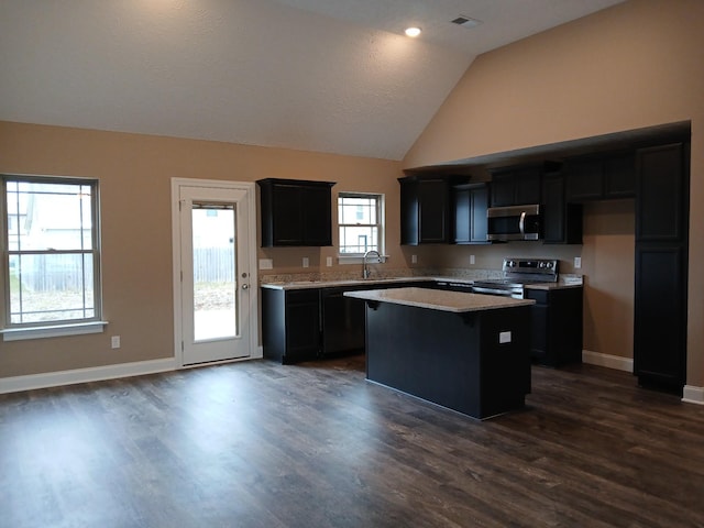 kitchen featuring dark cabinets, stainless steel appliances, dark wood-style flooring, a kitchen island, and vaulted ceiling