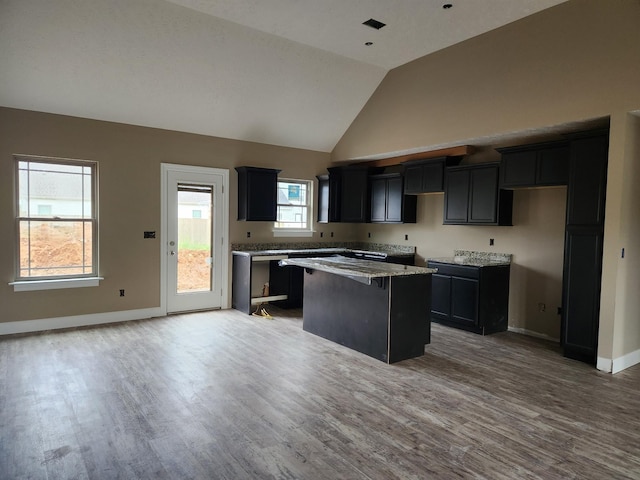 kitchen with wood finished floors, a kitchen island, light stone counters, and baseboards