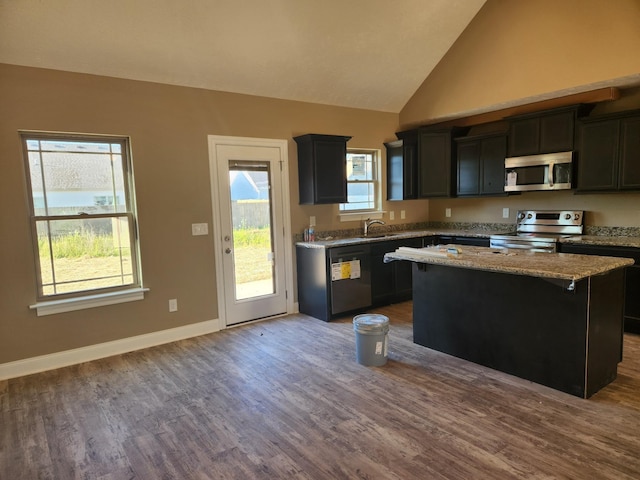 kitchen featuring dark wood-style flooring, a kitchen island, baseboards, appliances with stainless steel finishes, and light stone countertops