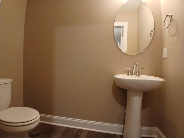 half bathroom with toilet, a sink, baseboards, and wood finished floors