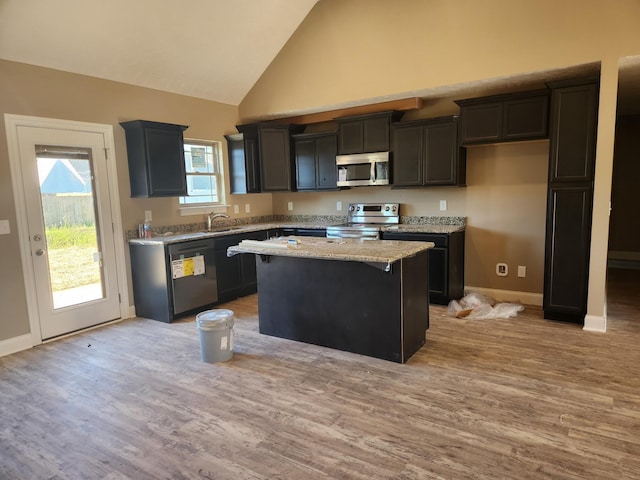 kitchen with light stone counters, appliances with stainless steel finishes, a sink, a kitchen island, and light wood-type flooring