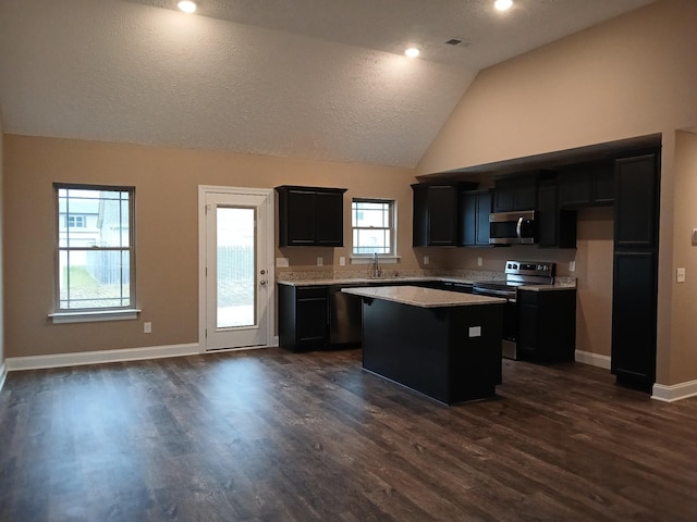 kitchen with stainless steel appliances, a sink, vaulted ceiling, light countertops, and a center island