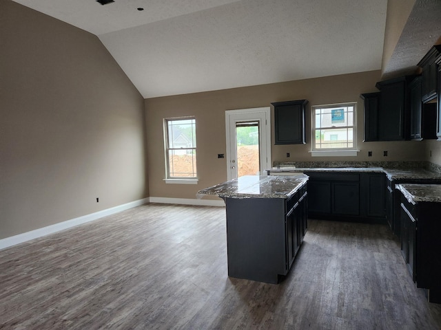 kitchen featuring light stone counters, a kitchen island, baseboards, vaulted ceiling, and dark wood finished floors