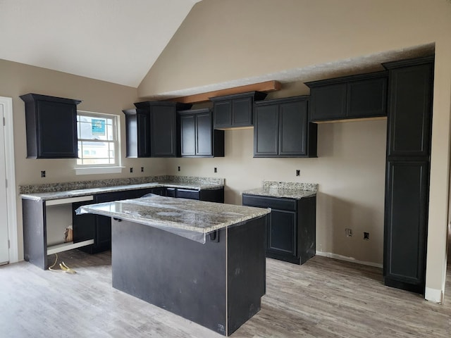 kitchen featuring high vaulted ceiling, a kitchen island, light wood-style floors, dark cabinetry, and light stone countertops