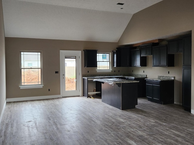 kitchen with stone counters, wood finished floors, baseboards, vaulted ceiling, and a center island