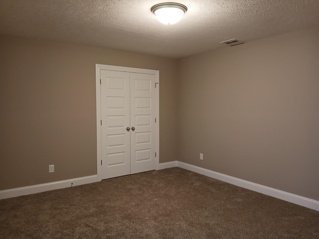 spare room featuring a textured ceiling, dark colored carpet, visible vents, and baseboards