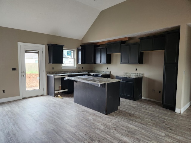 kitchen featuring light stone countertops, a kitchen island, baseboards, and wood finished floors