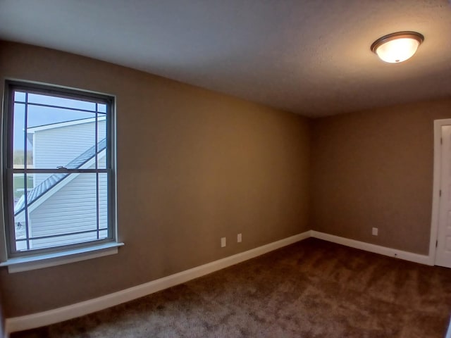 spare room featuring baseboards and dark colored carpet