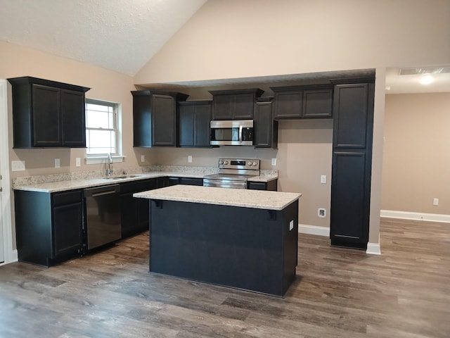 kitchen featuring stainless steel appliances, dark cabinetry, a kitchen island, and a sink