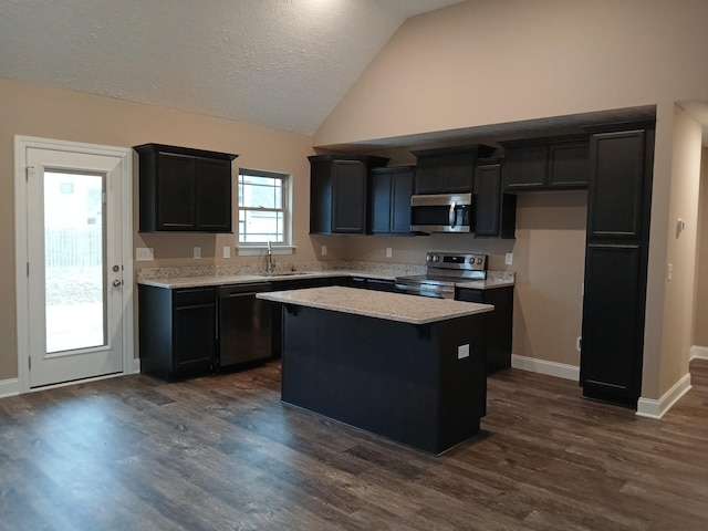 kitchen featuring dark cabinets, stainless steel appliances, vaulted ceiling, a center island, and dark wood finished floors