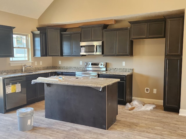 kitchen featuring lofted ceiling, appliances with stainless steel finishes, a kitchen island, light stone countertops, and light wood-type flooring