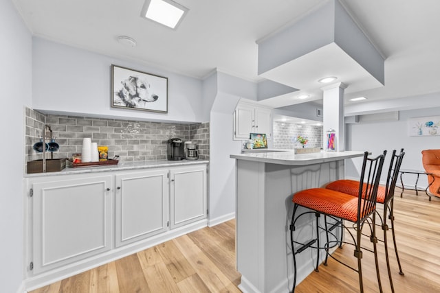 kitchen featuring white cabinets, light countertops, light wood-type flooring, tasteful backsplash, and a kitchen bar