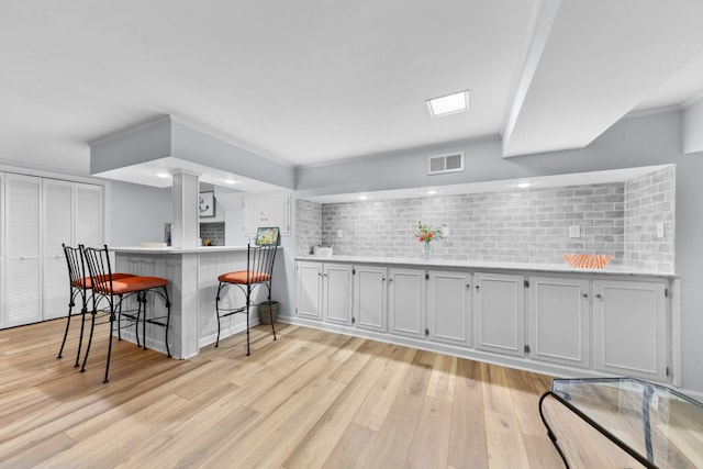 kitchen featuring a breakfast bar area, light countertops, visible vents, light wood-style floors, and a peninsula