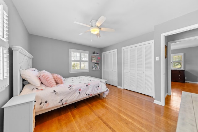 bedroom featuring light wood-style floors, multiple windows, baseboards, and two closets