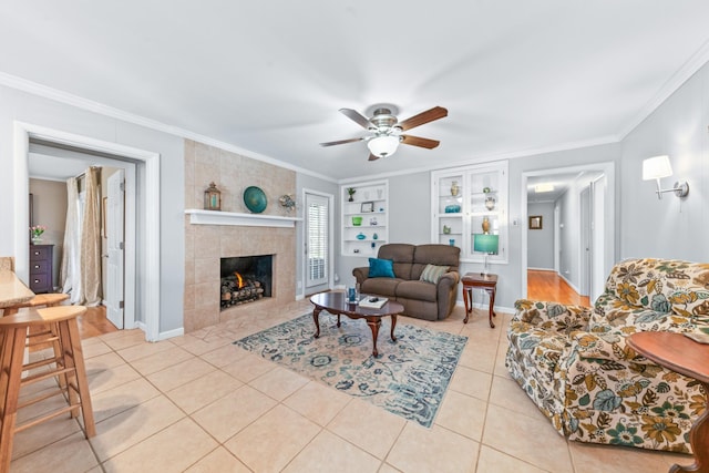 living room featuring a ceiling fan, ornamental molding, built in shelves, a fireplace, and light tile patterned flooring