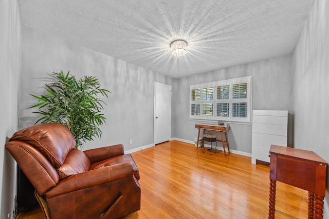 sitting room featuring light wood-style floors, baseboards, and a textured ceiling