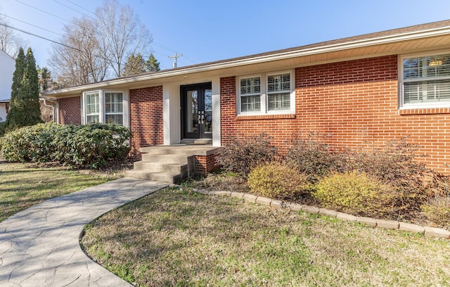 view of exterior entry with brick siding and a lawn