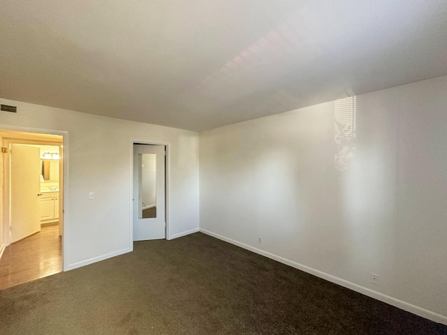 empty room with dark colored carpet, visible vents, and baseboards