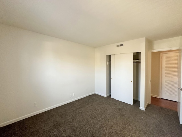 unfurnished bedroom featuring dark colored carpet, a closet, visible vents, and baseboards