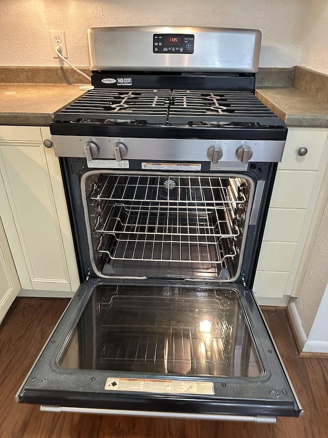 room details with stainless steel gas range, white cabinets, and a textured wall