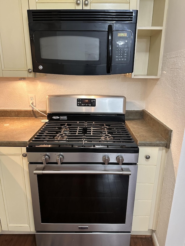 details with stainless steel range with gas cooktop, black microwave, a textured wall, and dark countertops