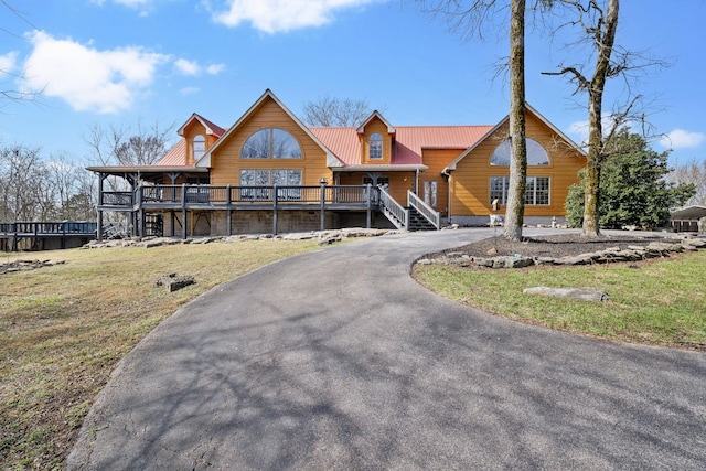 view of front of house featuring metal roof, driveway, a front yard, and a wooden deck