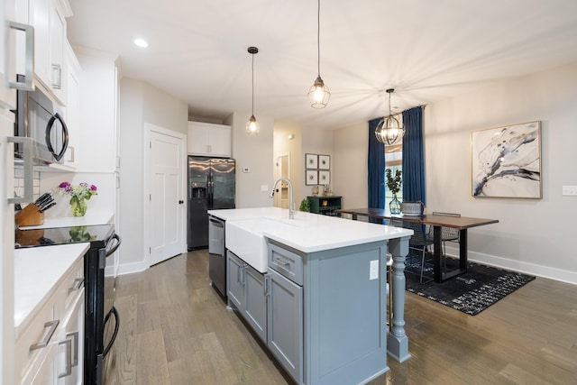 kitchen featuring pendant lighting, light countertops, a center island with sink, and white cabinets