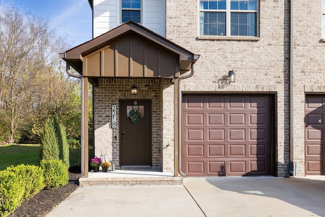 entrance to property with board and batten siding, brick siding, driveway, and a garage