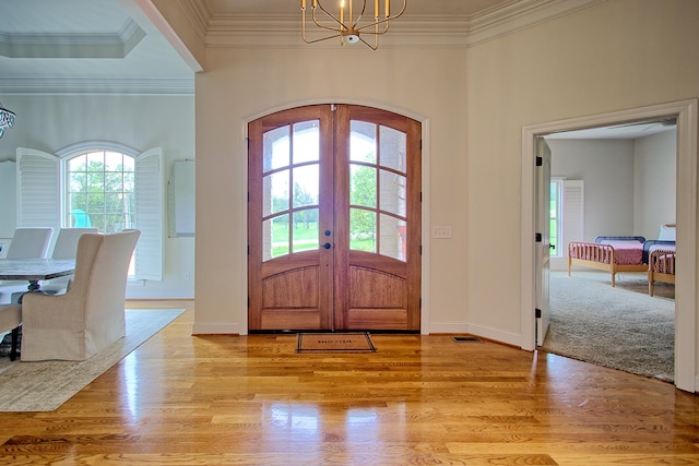 entrance foyer featuring light wood-type flooring, arched walkways, a notable chandelier, and french doors