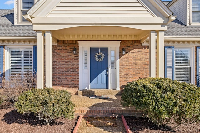 view of exterior entry with roof with shingles and brick siding