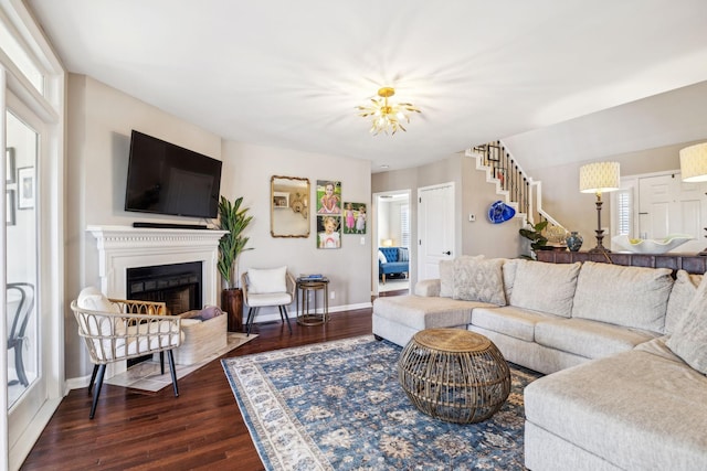 living area featuring dark wood-style floors, a lit fireplace, stairs, and baseboards