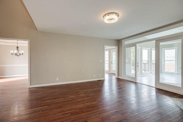 spare room featuring baseboards, dark wood-style flooring, and a notable chandelier