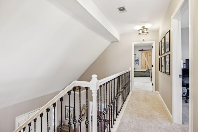 hall featuring a barn door, visible vents, baseboards, and light colored carpet