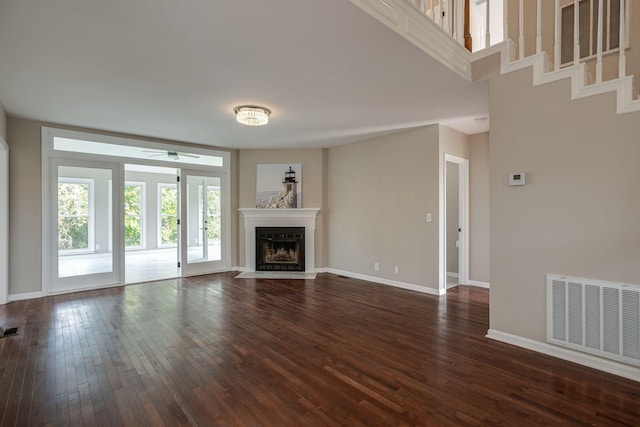 unfurnished living room featuring dark wood-style floors, visible vents, a fireplace with flush hearth, ceiling fan, and baseboards