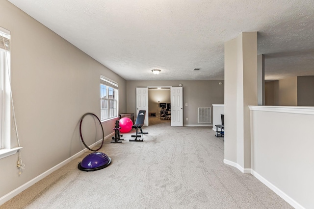 workout area with a textured ceiling, carpet, visible vents, and baseboards