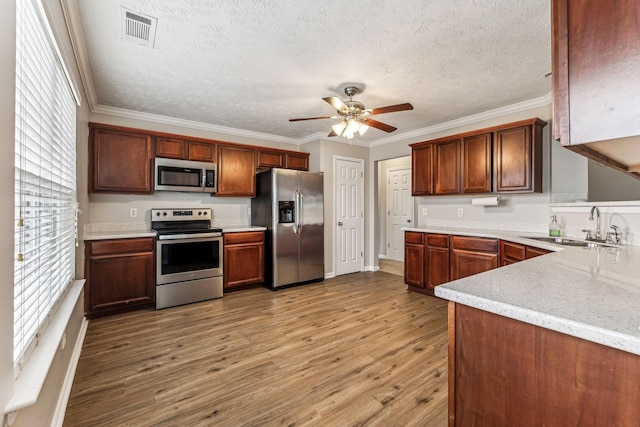 kitchen with a sink, visible vents, appliances with stainless steel finishes, light wood-type flooring, and crown molding