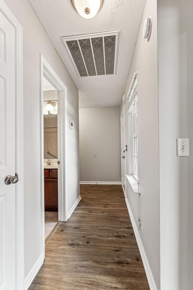 corridor featuring visible vents, a textured ceiling, baseboards, and wood finished floors