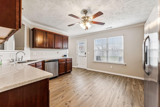 kitchen featuring stainless steel appliances, ornamental molding, a sink, and light wood-style floors