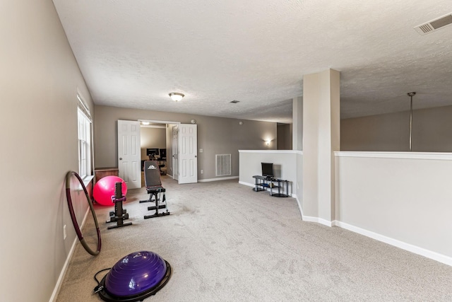 workout area with carpet floors, visible vents, a textured ceiling, and baseboards